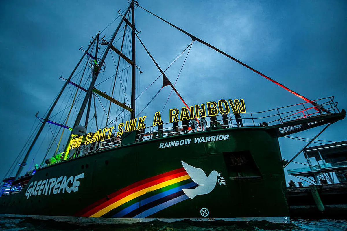 An image of Greenpeace’s ship the ‘Rainbow Warrior’. The Rainbow Warrior is an undisputed icon, synonymous with breaking boundaries and fearless campaigning. The ship is a tall mast ship. There are activists along the length of the ship behind the words ‘You can’t sink a rainbow’. There is a rainbow and a dove with an olive branch painted across the side of the ship.